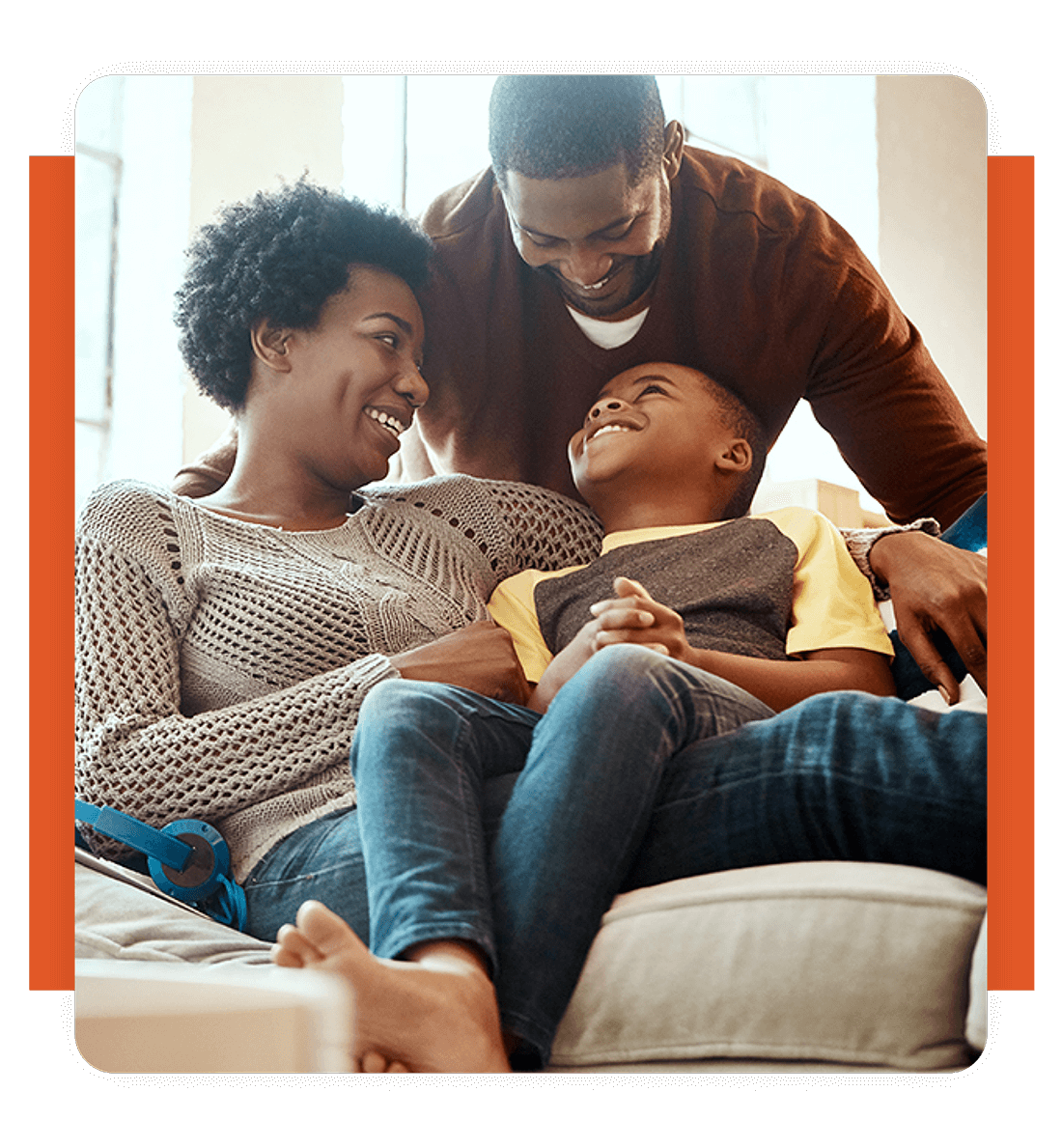 A smiling family of three sitting on a couch, with the parents embracing their child